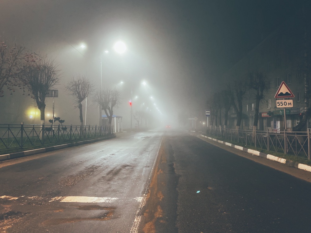 Illustrative stock photograph of an empty street under streetlights in dense fog at night