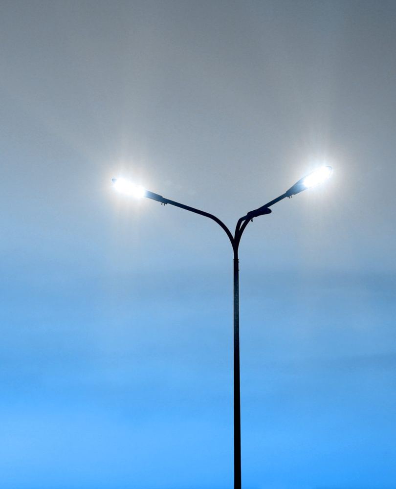 A row of LED street lights switched on against a blue-grey dusk sky